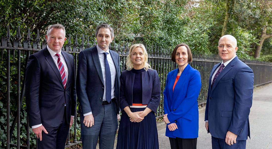 Five people standing in a laneway with green hedges behind them.