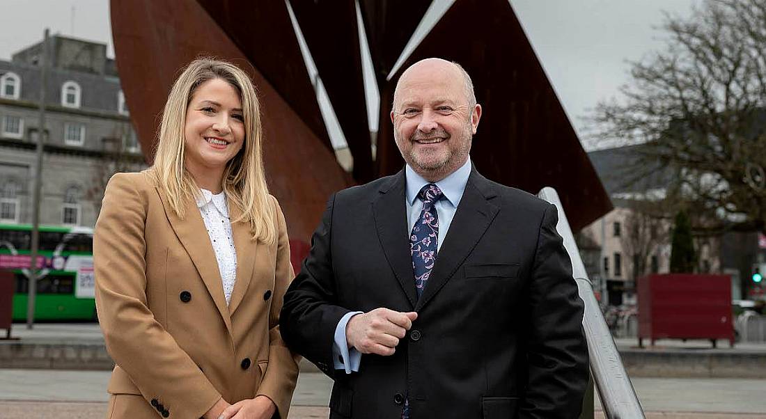 A woman and a man stand side by side smiling at the camera.