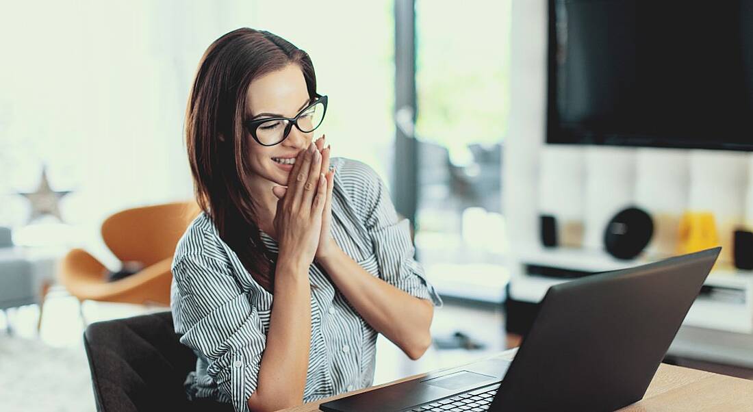 A woman sitting at a table looking at a laptop and smiling because she just applied for a job.