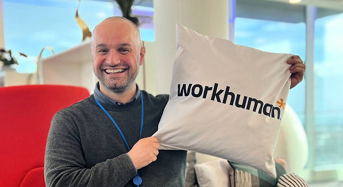 A man smiling while holding up a square cushion that says Workhuman on it.