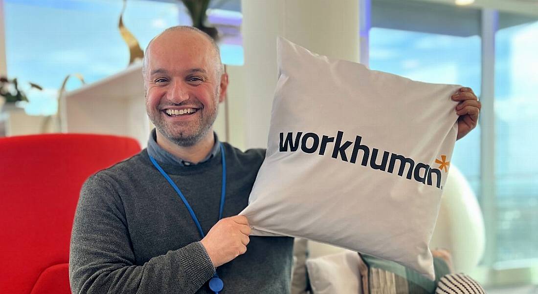 A man smiling while holding up a square cushion that says Workhuman on it.