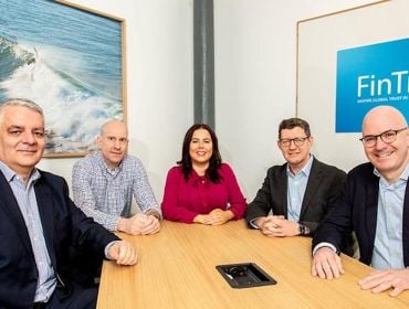 Four men and one woman sit around a boardroom table smiling at the camera. A sign that says FinTru is on the wall behind them.