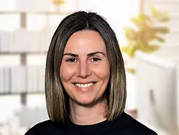 A woman with long brown hair wearing a dark blazer smiles at the camera. She is Karen MacGregor.