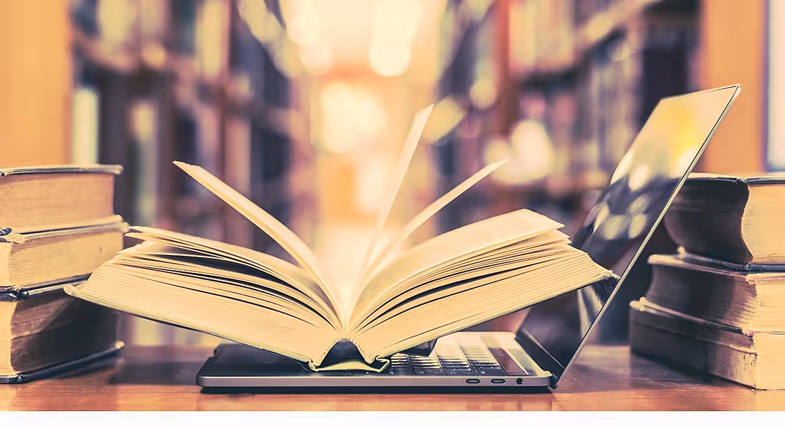 Books sitting beside and on top of a laptop in a library in a digital literacy concept.