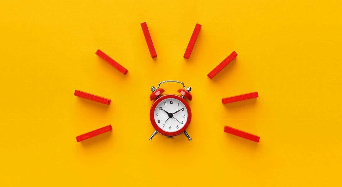 A red alarm clock with red dominoes arranged around it in a semicircle. Yellow background.