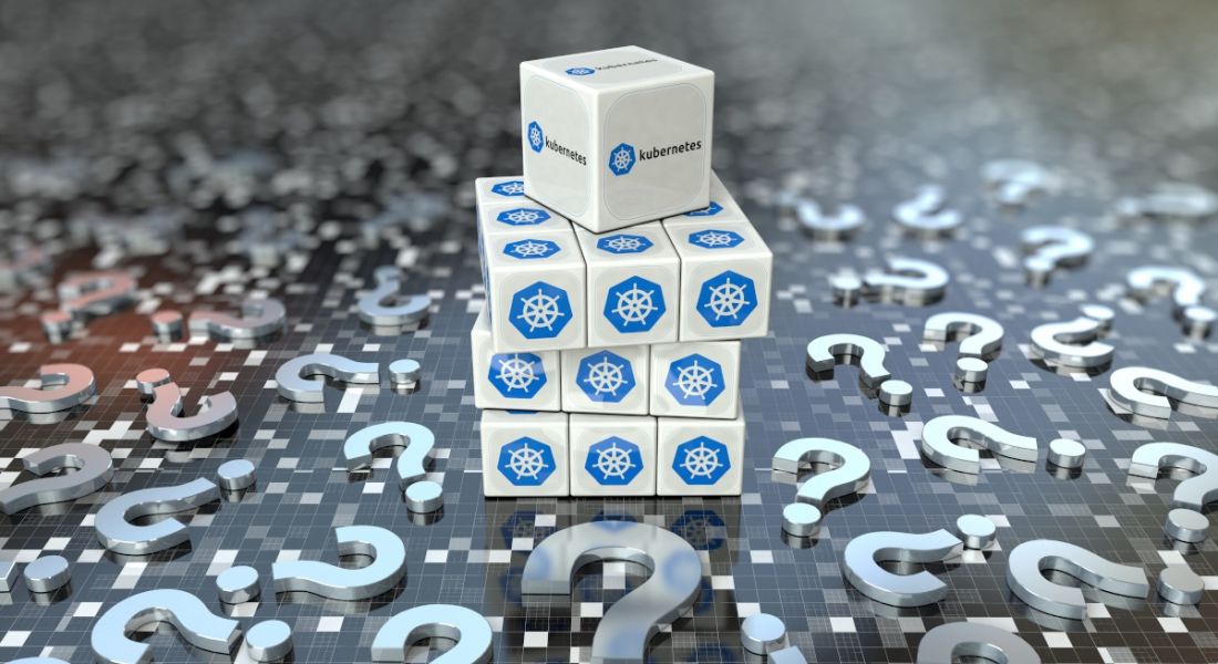 Stack of cubes with the Kubernetes logo on them resting on a grey surface with question marks littered around it.