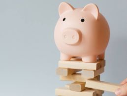 A piggy bank is standing on a dark wooden table against a pink and purple background.