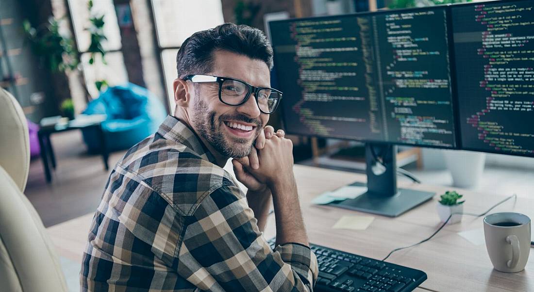 Man working as a software engineer sitting at a desk in front of several computer monitors displaying code.