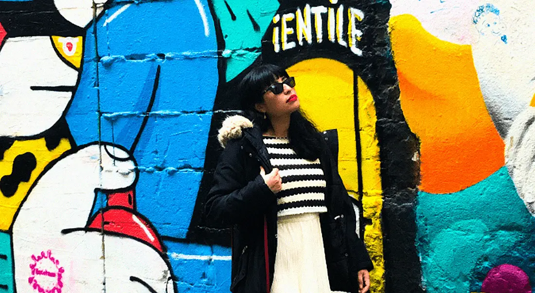 A woman stands against a wall with graffiti art on it. She is Erika Herrero, a senior data engineer at Fidelity Investments.