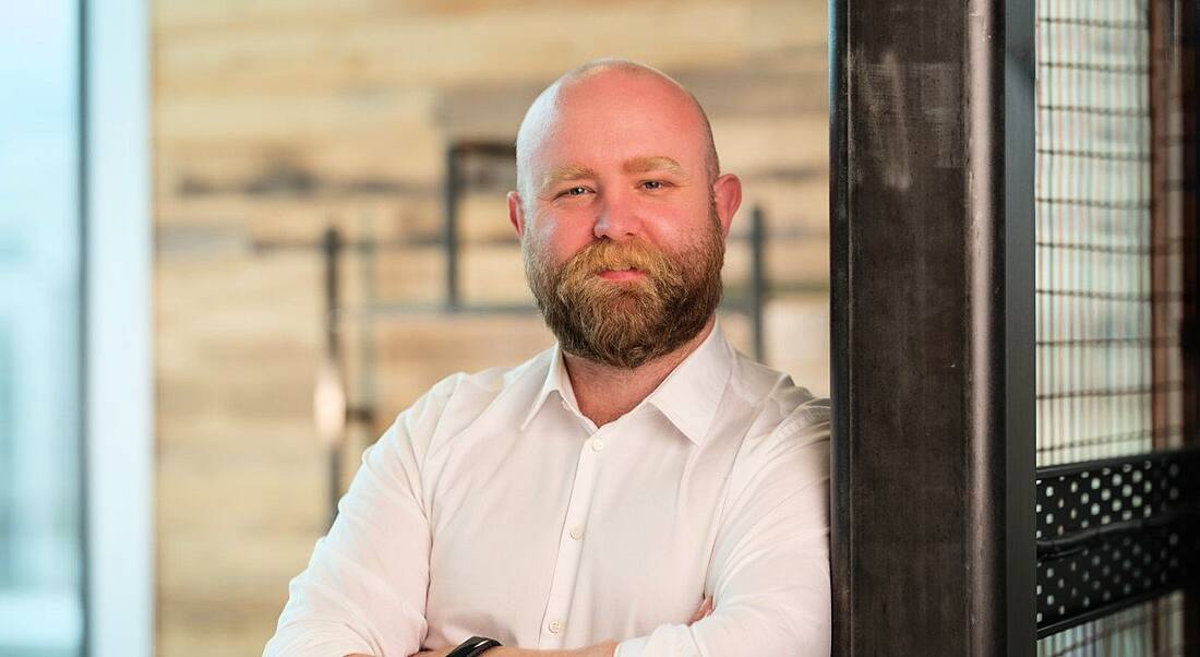 A man stands smiling at the camera with his arms folded. He is Killian Walsh.