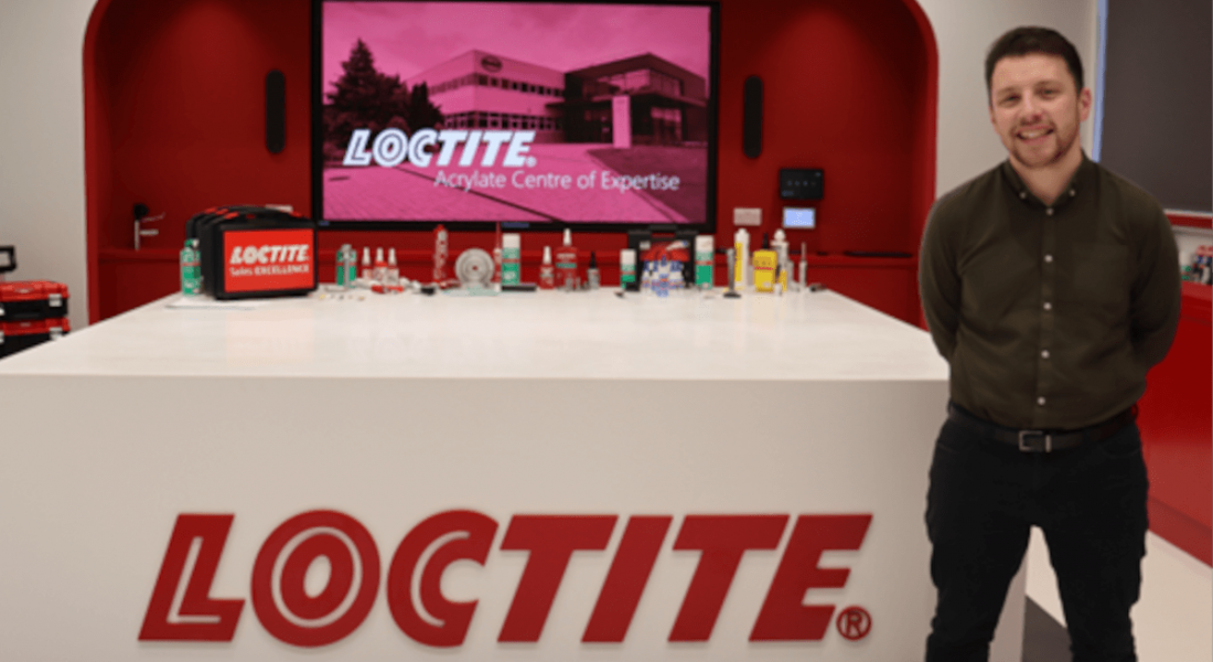 A man stands next to a desk that has the Loctite logo on it. He is Stephen Fearon, an application engineer at Henkel.