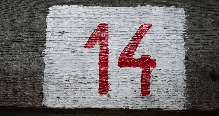 A red number 14 painted on a wooden plank.