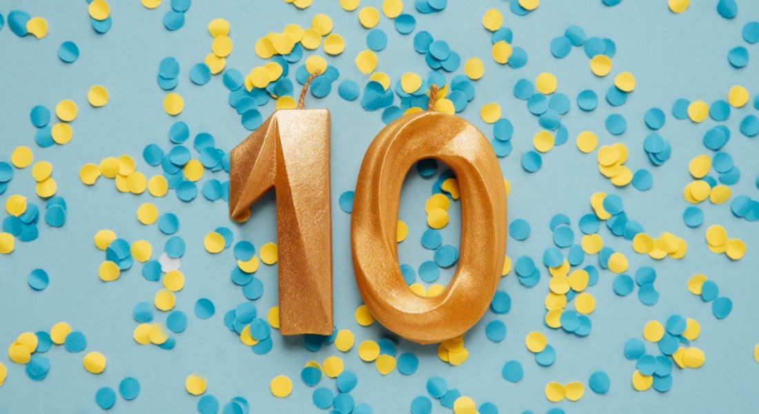 Two gold candles showing the number 10 lying on a blue background covered in yellow and blue confetti.