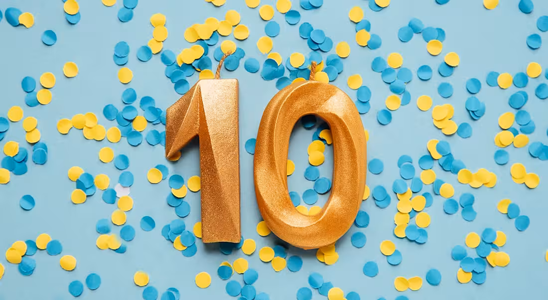 Two gold candles showing the number 10 lying on a blue background covered in yellow and blue confetti.