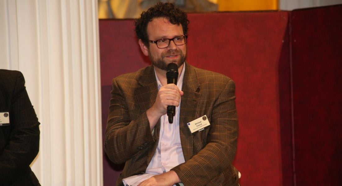 A man with dark hair, a beard and glasses sits while holding a microphone. He is Michael Dascal, director of quantum product management at Fidelity Investments.