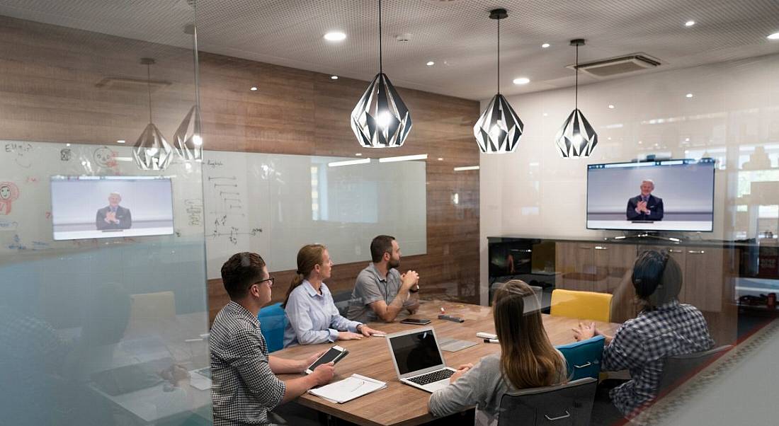 Employees seated around a table in an office using video conferencing tools.