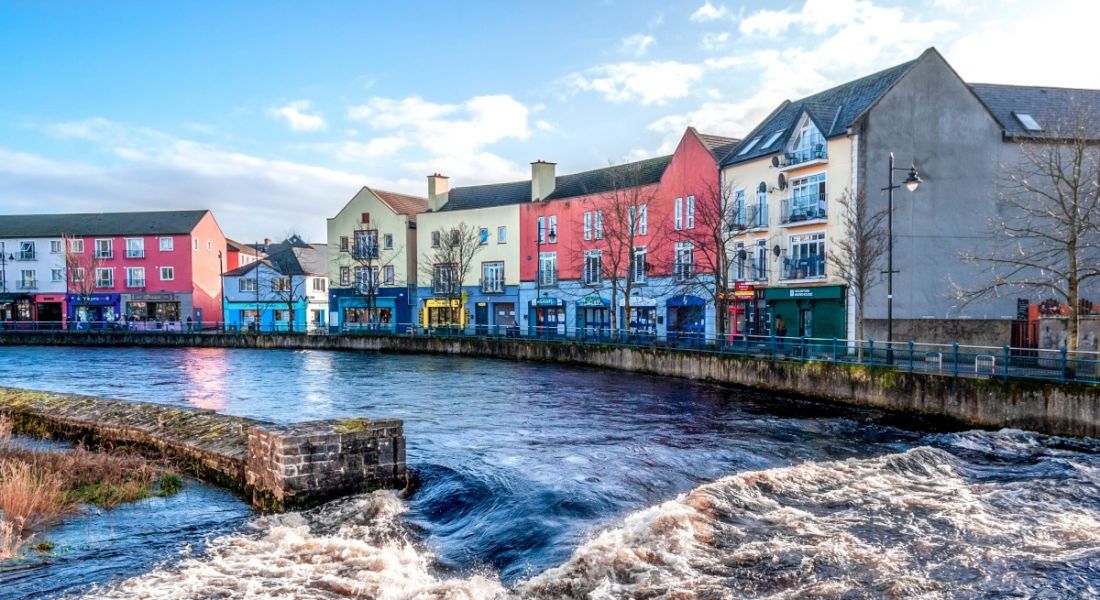 A view of Sligo town with colourful buildings and a river flowing through it and blue sky in the background.