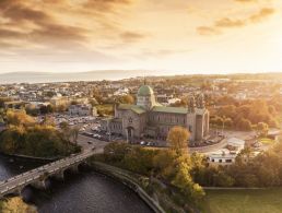 An aerial view of Galway cathedral at sunset with the city visible around it and the sea in the background.