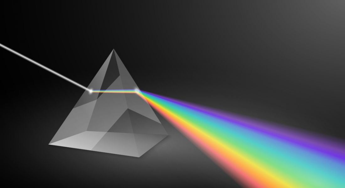 A prism expands light into beams of rainbow colour against a dark background.