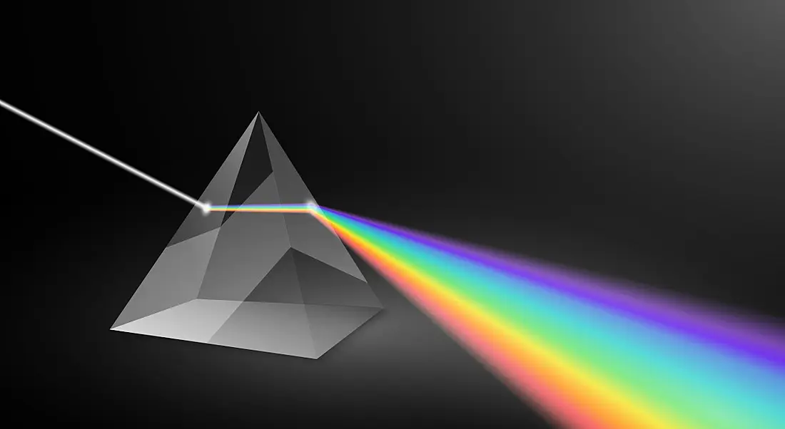 A prism expands light into beams of rainbow colour against a dark background.