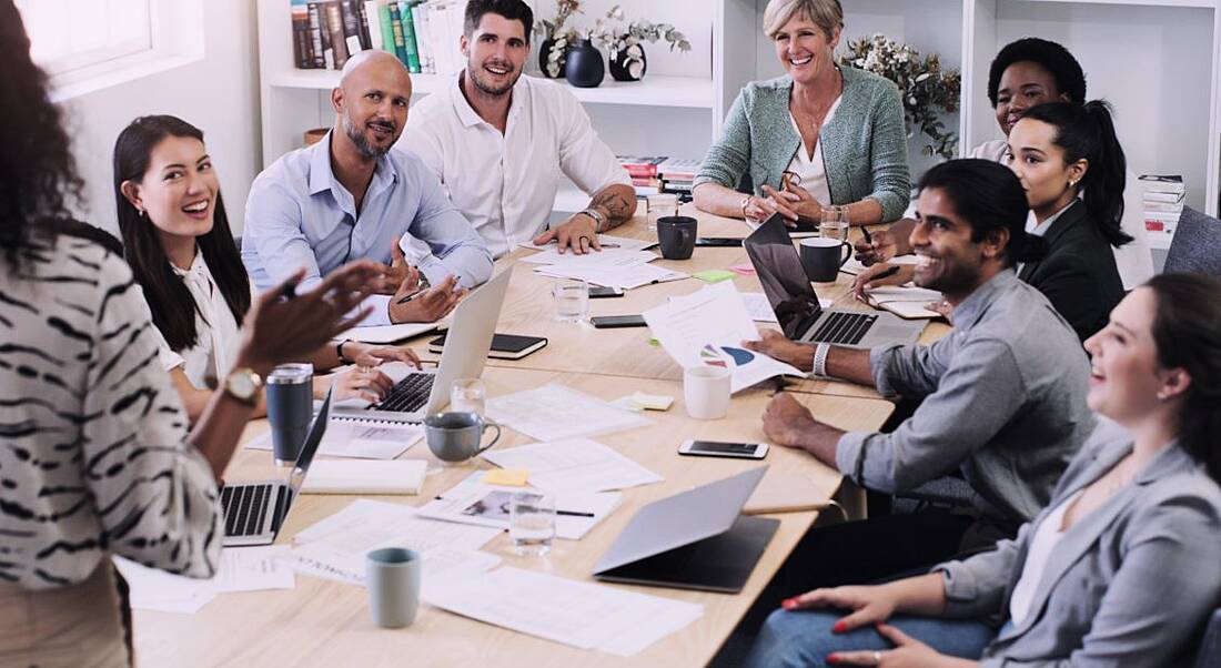 A group of start-up employees gathered around a table in an office with documents, laptops and coffee cups.