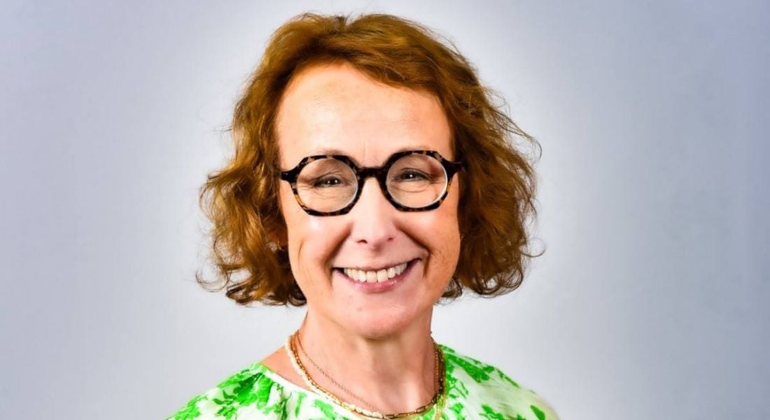 A woman with brown hair and glasses smiles at the camera in front of a grey background. She is Katherine Conway, global head of inclusion and cultural initiatives at Aon.