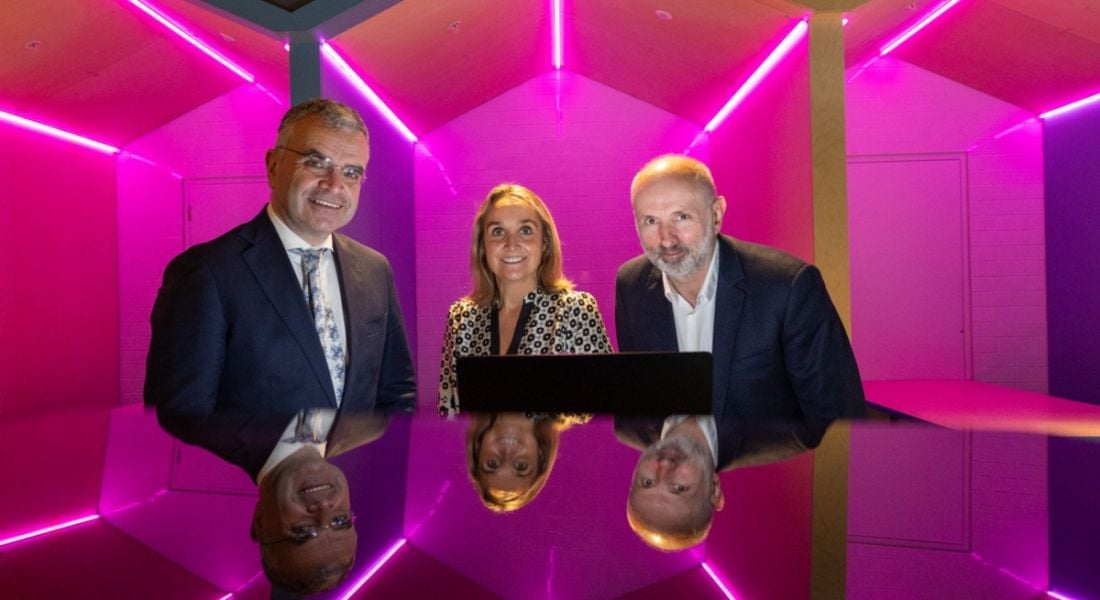 Dara Calleary and two people from Microsoft Ireland in a room with very vivid pink lighting.