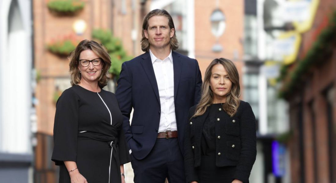 Three people standing in front of some red brick buildings that are out of focus celebrating the jobs announcement by Spectrum.Life.