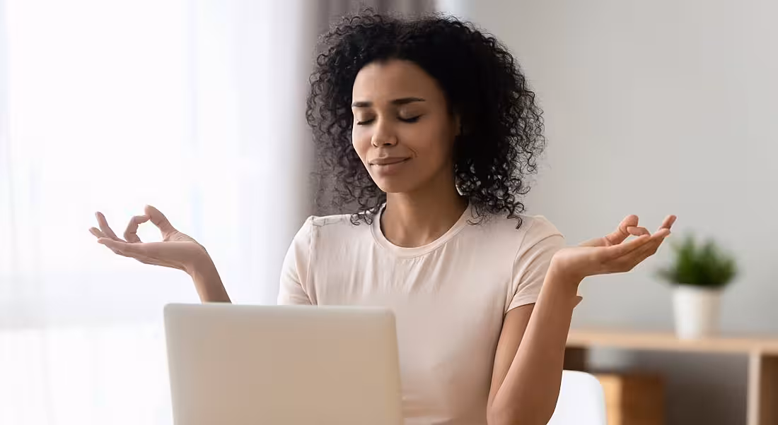 Woman meditating at her desk in front of a laptop in a how to be your best self at work concept.