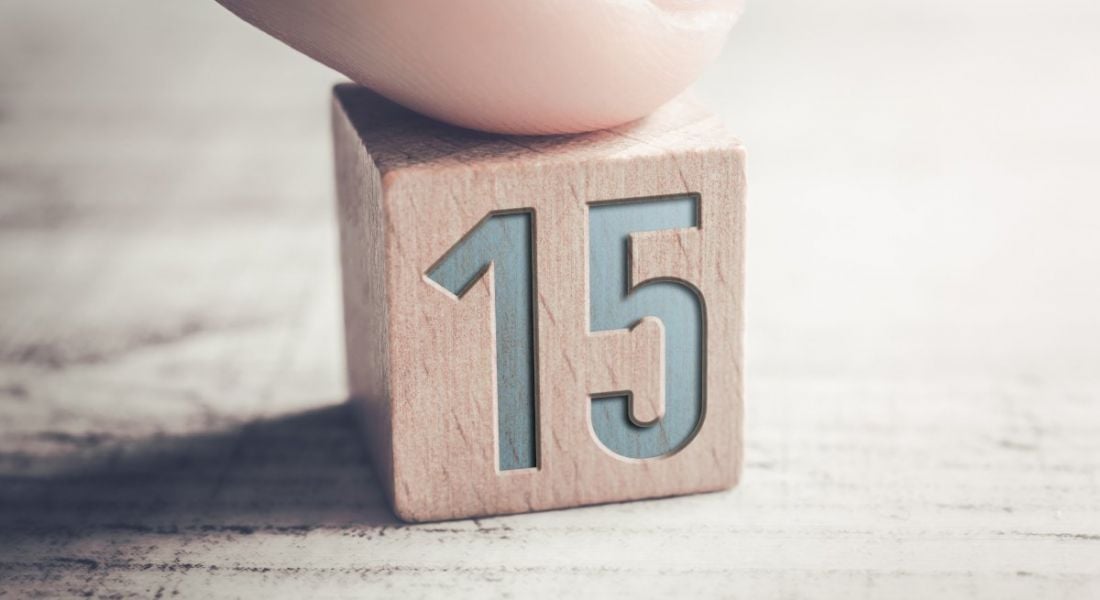 Close up of a person's finger on a wooden block with the number 15 on it.