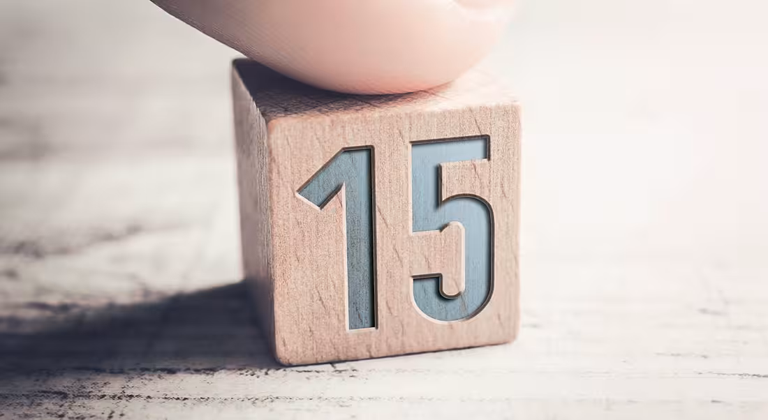 Close up of a person's finger on a wooden block with the number 15 on it.
