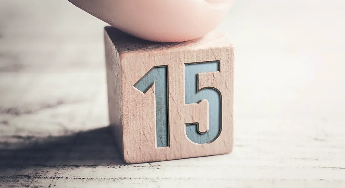 Close up of a person's finger on a wooden block with the number 15 on it.