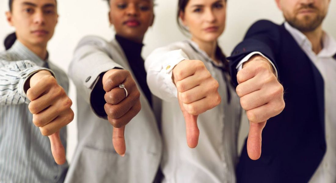 Two men and two women in business clothing all giving a thumbs down gesture with their right hands.