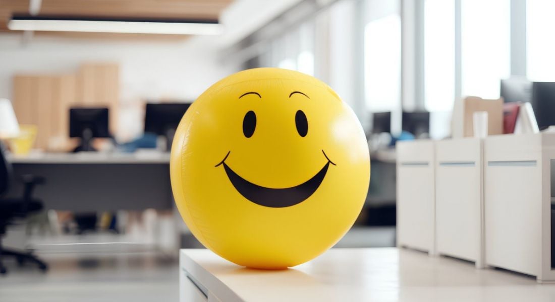 Workplace wellbeing concept with a yellow ball with a smiley face on it in an office.