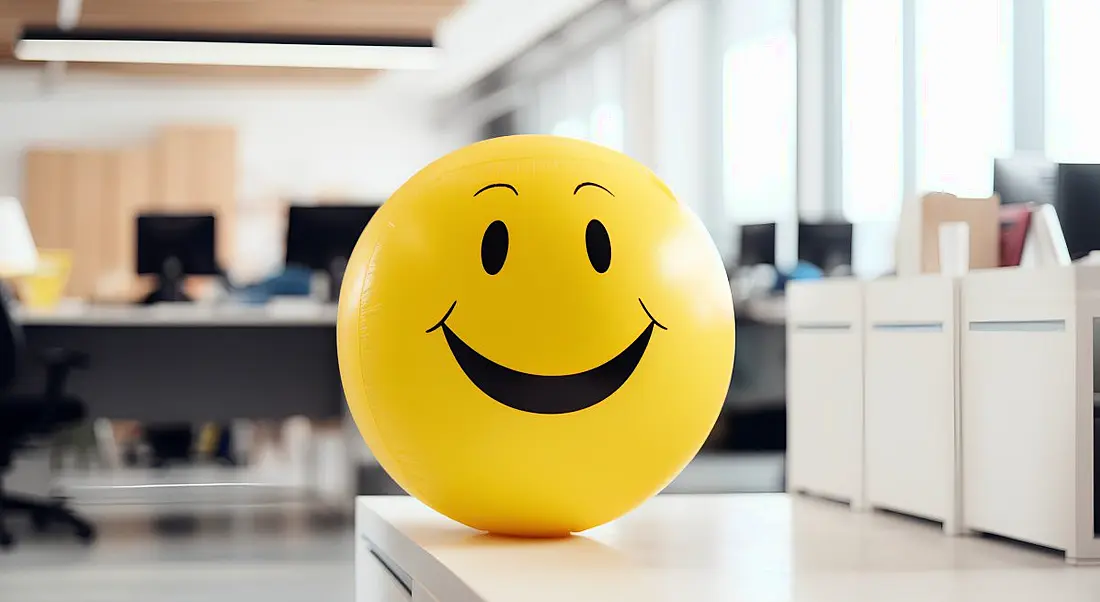 Workplace wellbeing concept with a yellow ball with a smiley face on it in an office.