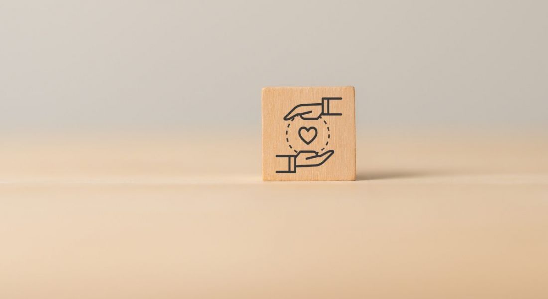 A wooden block with two hands holding a heart signifying customer and employee experiences. The background is a plain wooden surface.