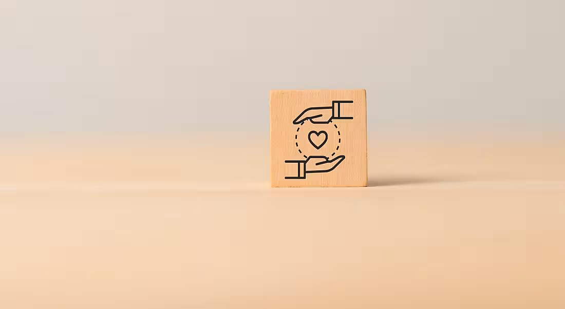 A wooden block with two hands holding a heart signifying customer and employee experiences. The background is a plain wooden surface.