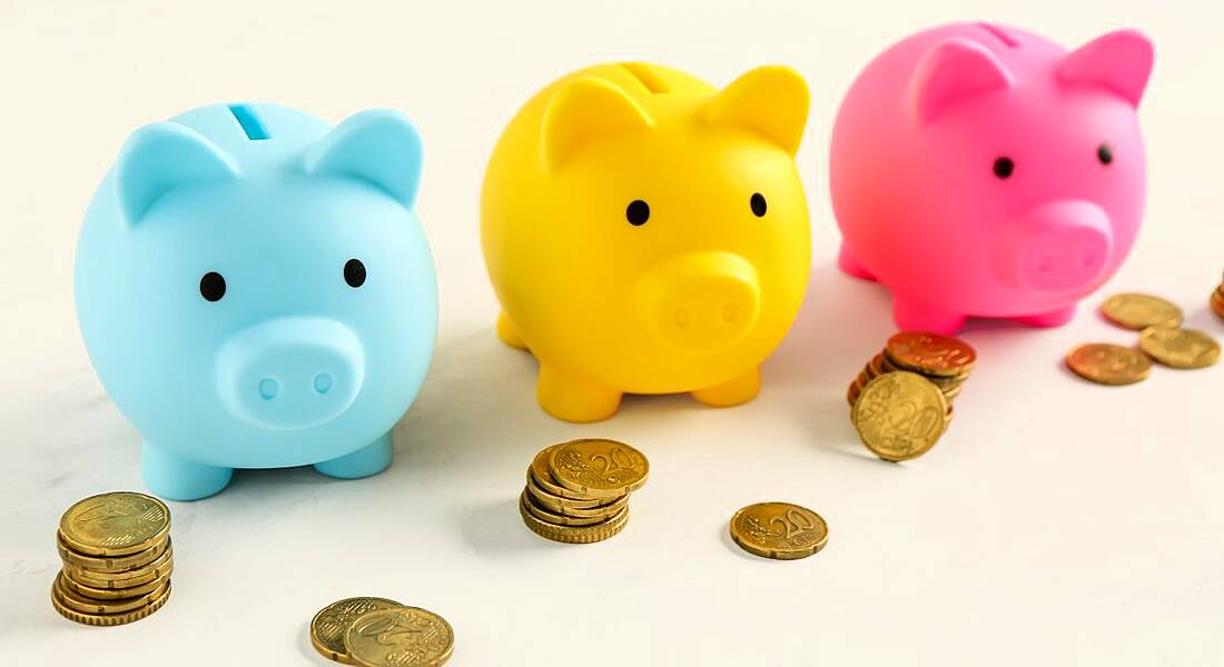 Three brightly coloured piggy banks with gold coins scattered around them on a very pale yellow background.