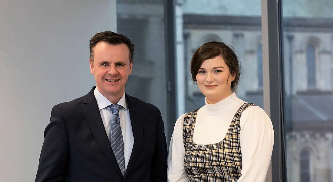 A man in a suit stands next to a young woman smiling at the camera.