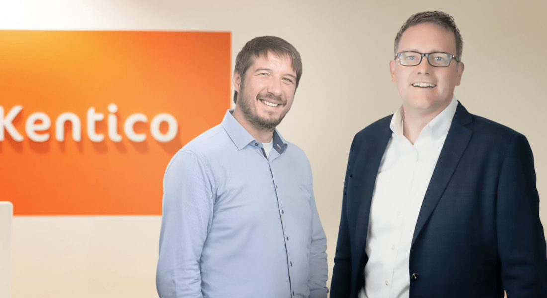 Two men standing together in front of a wall that has the Kentico logo on it. They are part of Kentico and Granite Digital.