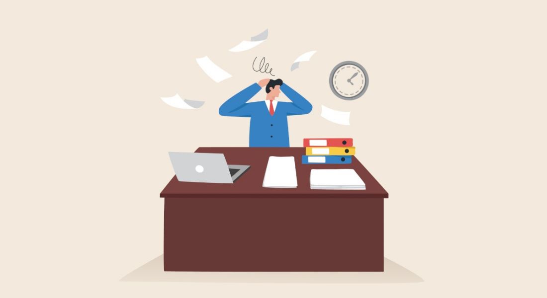 An illustration of a man at work at his desk throwing his hands in the air while multiple papers fly and hover around him. There are folders and a laptop on his desk and a clock on the wall behind him. This image symbolises stress.