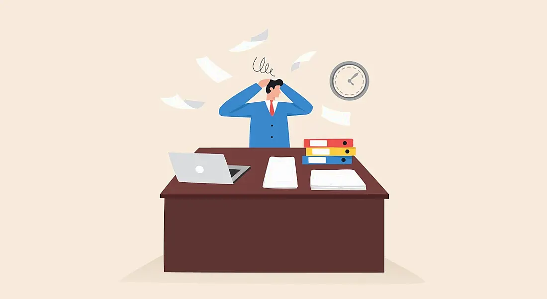 An illustration of a man at work at his desk throwing his hands in the air while multiple papers fly and hover around him. There are folders and a laptop on his desk and a clock on the wall behind him. This image symbolises stress.