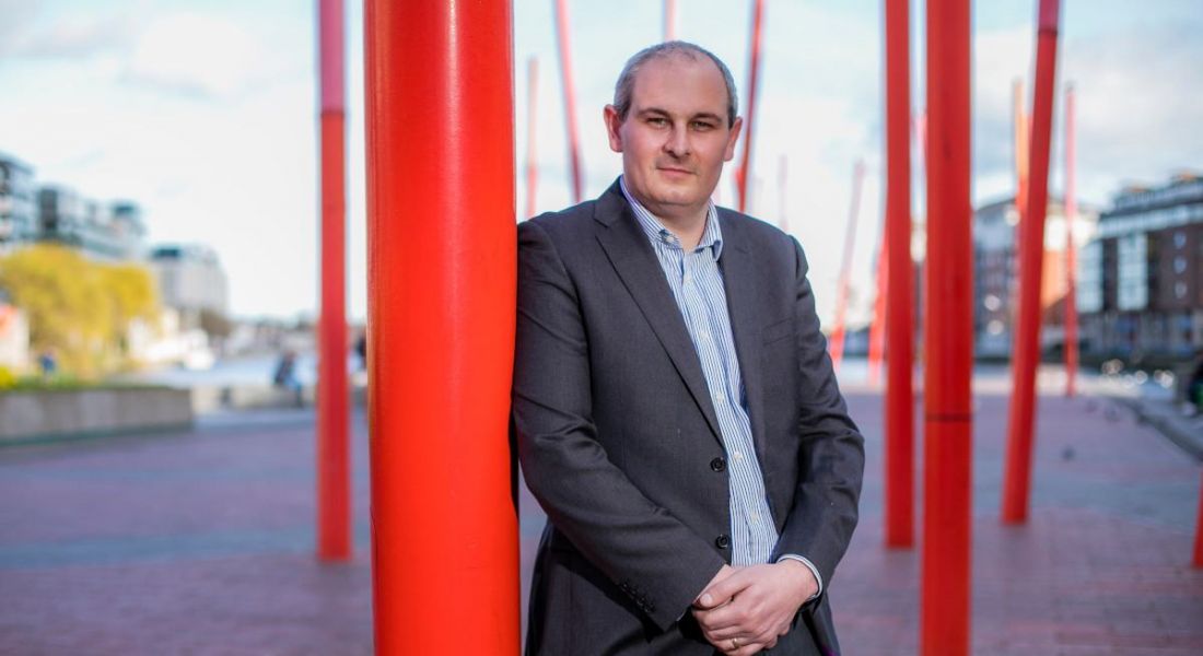 Mark Cockerill of ServiceNow standing leaning up against a red sculpture statue outside in Dublin.