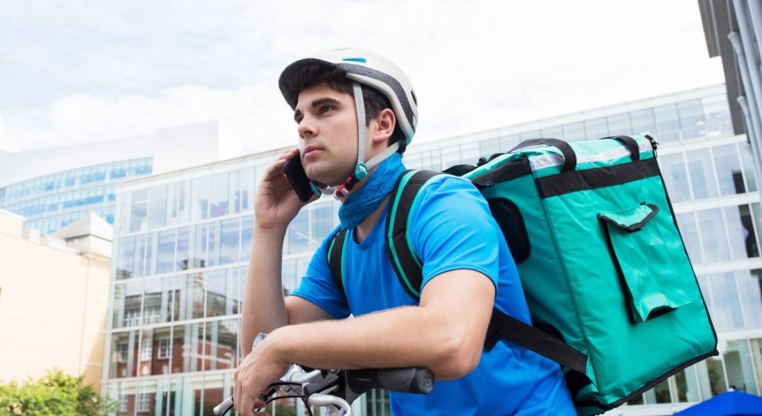 Gig economy worker on a bicycle with his phone in his hand getting ready to deliver something.