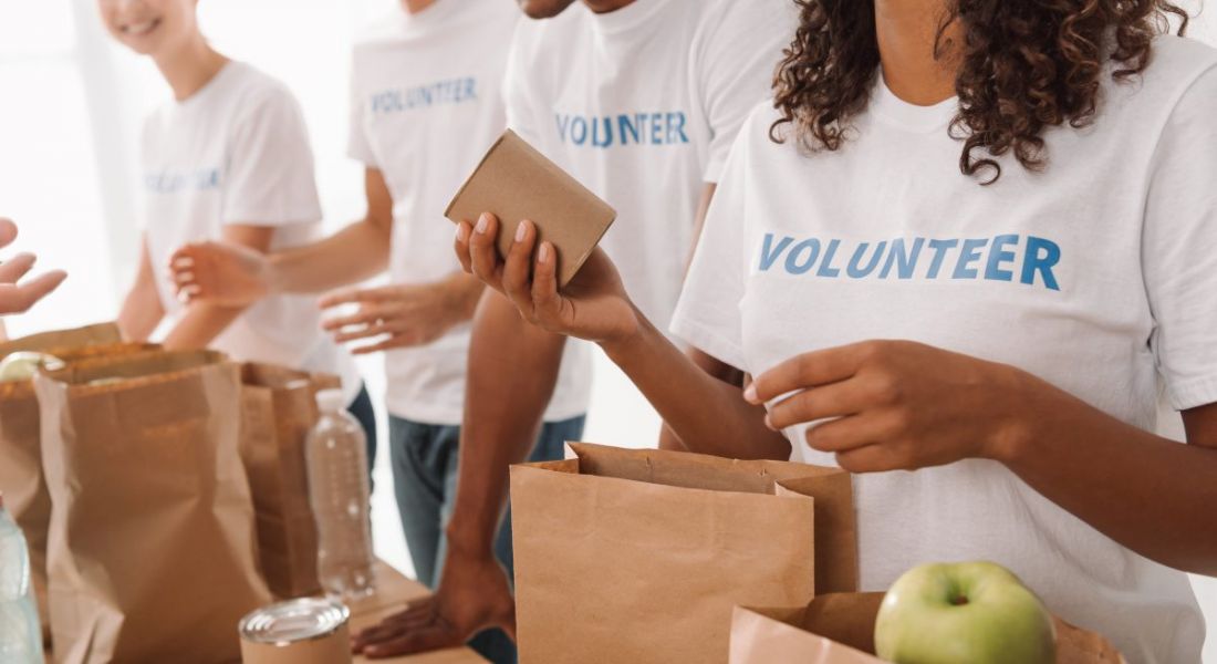 CSR in communities concept showing employees wearing t-shirts labelled volunteer packing paper bags with food for charity.