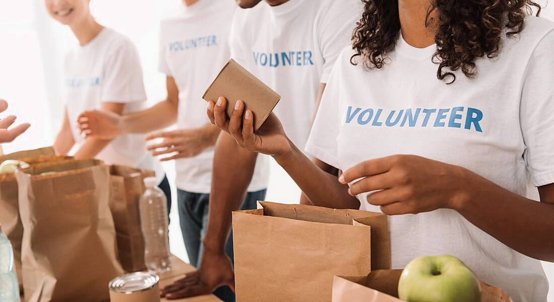 CSR in communities concept showing employees wearing t-shirts labelled volunteer packing paper bags with food for charity.