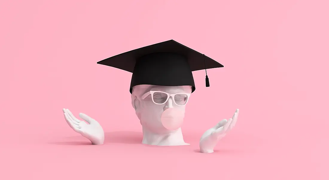 A statue of a head wearing a graduate cap and glasses blowing bubblegum on a pink background.