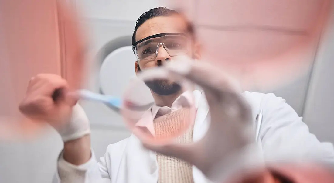 A biopharma worker examining a Petri dish and wearing lab gear.