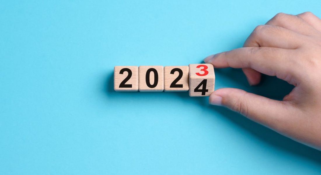 Person's hand turning a cube on a calendar from 2023 to 2024. Blue background.