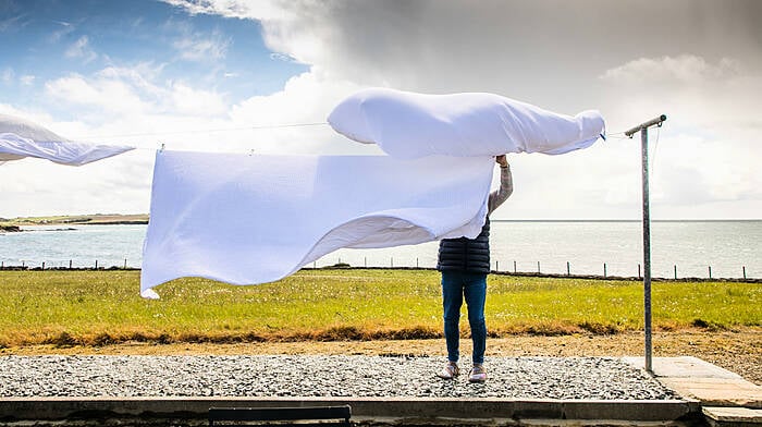 On a blustry day a woman brings in the sheets from the line, before the onset of heavy showers outside Kinsale.   (Photo: David Creedon)